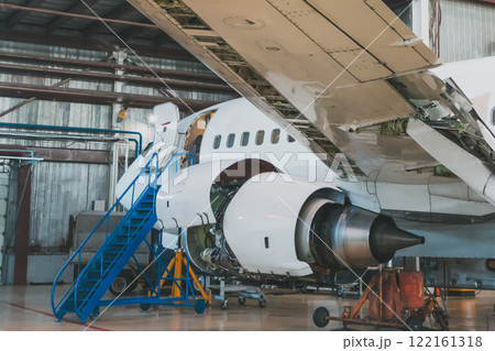 Close-up of a white passenger jetliner with engine open in the airplane hangar. Aircraft under maintenance. Checking mechanical systems for flight operations 122161318