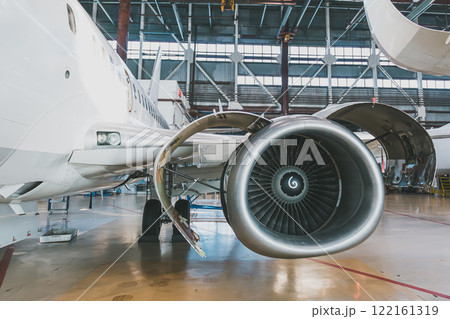 White passenger jet plane in the aviation hangar. Aircraft under maintenance. Checking mechanical systems for flight operations 122161319