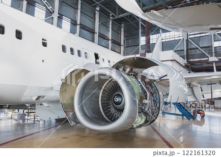 White passenger plane in the aviation hangar. Airplane under maintenance. Checking mechanical systems for flight operations 122161320