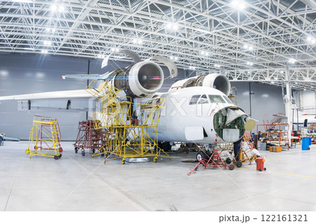 White transport aircraft in the hangar. Airplane under maintenance. Checking mechanical systems for flight operations 122161321