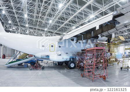 White transport airplane in the hangar. Aircraft under maintenance. Checking mechanical systems for flight operations White transport airplane in the hangar. Aircraft under maintenance. Checking mechanical systems for flight operations 122161325