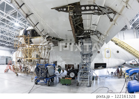 White transport aircraft in the hangar. Airplane under maintenance. Checking mechanical systems for flight operations White transport aircraft in the hangar. Airplane under maintenance. Checking mechanical systems for flight operations 122161328