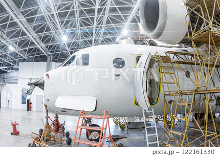 Close-up white transport airplane in the hangar. Aircraft under maintenance. Checking mechanical systems for flight operations Close-up white transport airplane in the hangar. Aircraft under maintenance. Checking mechanical systems for flight operations 122161330