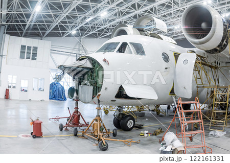 Close-up of white transport aircraft in the hangar. Airplane under maintenance. Checking mechanical systems for flight operations 122161331