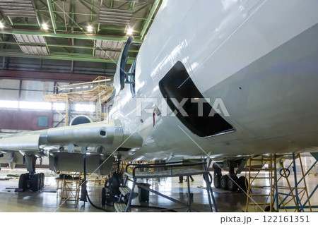 White passenger aircraft in the hangar. Airplane under maintenance. Checking mechanical systems for flight operations 122161351