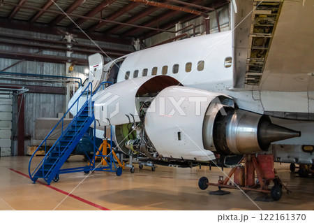 White passenger aircraft in the aviation hangar. Jetliner under maintenance. Checking mechanical systems for flight operations 122161370