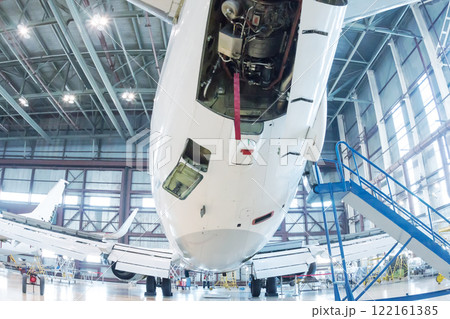 White passenger aircraft in the hangar. Airplane under maintenance. Checking mechanical systems for flight operations 122161385