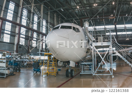 White passenger airliner in the aircraft hangar. Airplane under maintenance. Checking mechanical systems for flight operations White passenger airliner in the aircraft hangar. Airplane under maintenance. Checking mechanical systems for flight operations 122161388