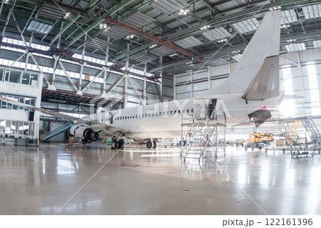 White passenger airliner in the aviation hangar. Airplane under maintenance. Checking mechanical systems for flight operations White passenger airliner in the aviation hangar. Airplane under maintenance. Checking mechanical systems for flight operations 122161396