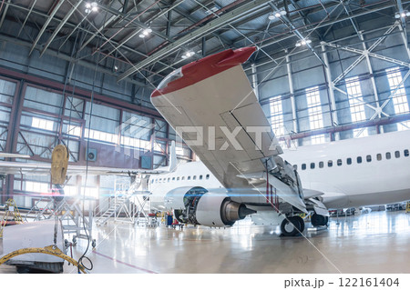 White passenger aircraft in the aviation hangar. Airplane under maintenance. Checking mechanical systems for flight operations White passenger aircraft in the aviation hangar. Airplane under maintenance. Checking mechanical systems for flight operations 122161404