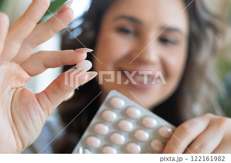 A young beautiful woman holds a pink round contraceptive hormonal pill in her hands. The girl is going to take the medicine A young beautiful woman holds a pink round contraceptive hormonal pill in her hands. The girl is going to take the medicine 122161982
