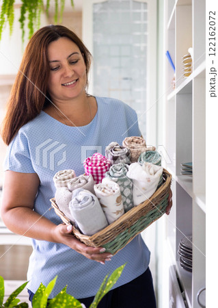 Smiling housewife female kitchen textile towels roll in whicked basket cabinet storage organizing Smiling housewife female kitchen textile towels roll in whicked basket cabinet storage organizing 122162072