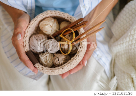 A woman in stylish clothes holds a crocheted basket with skeins of cotton yarn in natural tones  122162156