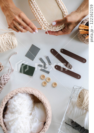 Women's hands knitting a basket from beige yarn. Crochet hooks. Skeins of yarn 122162159