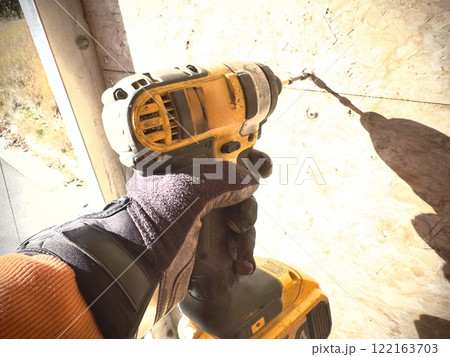 a worker in a glove tightens a screw using a screwdriver a worker in a glove tightens a screw using a screwdriver 122163703