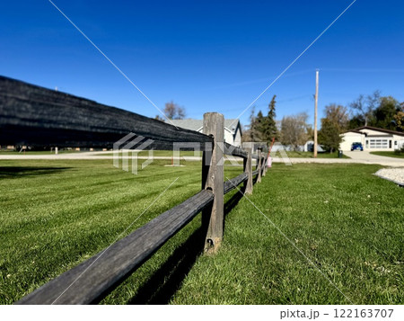 wooden fence along green lawn with houses and clear blue sky in background wooden fence along green lawn with houses and clear blue sky in background 122163707