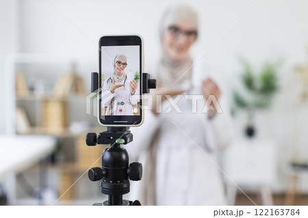 Muslim woman blogger recording video about medicine treatment. Focus on education, communication. Female adult wearing hijab creates informative content. 122163784