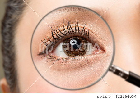 カラーコンタクトレンズを装着した若い女性の目をルーペで拡大している。 122164054