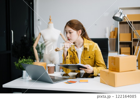 Young business owner woman prepare parcel box and standing check online orders for deliver to customer on tablet, laptop 122164085