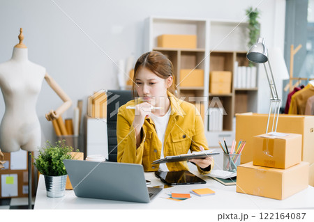 Young business owner woman prepare parcel box and standing check online orders for deliver to customer on tablet, laptop 122164087