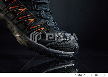 Close-up of waterproof black hiking boot with orange accents and water droplets. Rugged trekking shoe on dark background. Footwear for exploration and outdoor activities Close-up of waterproof black hiking boot with orange accents and water droplets. Rugged trekking shoe on dark background. Footwear for exploration and outdoor activities 122164134