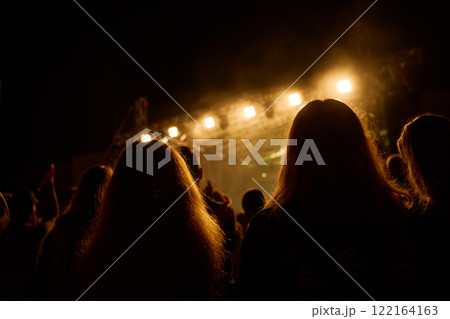 Vibrant live concert scene with band performing on stage under bright spotlights. People enjoying live music performance at an outdoor concert Vibrant live concert scene with band performing on stage under bright spotlights. People enjoying live music performance at an outdoor concert 122164163