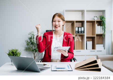 Confident Asian woman with a smile standing holding notepad and tablet at the ffice. Confident Asian woman with a smile standing holding notepad and tablet at the ffice. 122164384