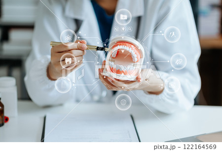 Dentist sitting at table with jaw samples tooth model and working with tablet and laptop in dental office 122164569