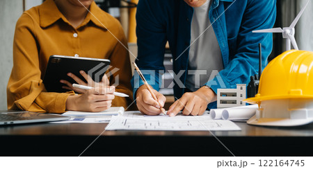 Two colleagues discussing data working and tablet, laptop with architectural project about wind energy at construction site at desk in modern office 122164745