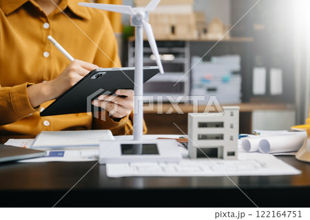 Alternative energy engineer pointing to a solar power panel and discuss with  business colleague team for the future power in the office 122164751