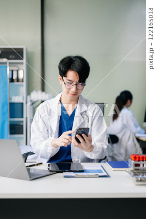 Confident young male doctor in white medical uniform sit at desk working on computer 122165018