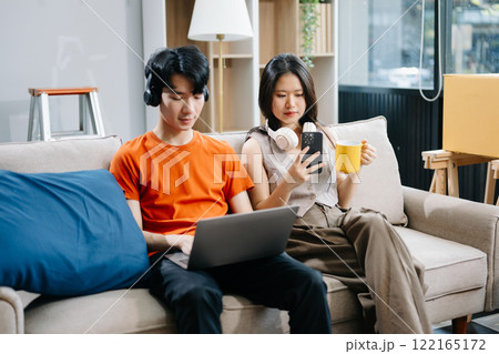 Smiling couple enjoying casual moments on the couch with a laptop, showcasing teamwork, laughter, and a relaxed 122165172