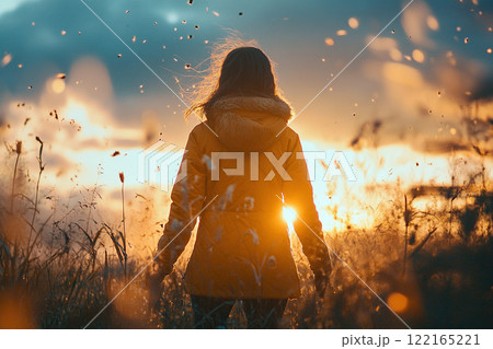 Rear view of a girl in a jacket standing in a field of dry grass at golden hour. Generated by artificial intelligence 122165221