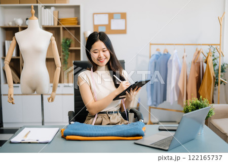Successful fashion designer. Attractive young asian woman with smile while standing in workshop. 122165737