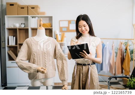 Successful fashion designer. Attractive young asian woman with smile while standing in workshop. 122165739