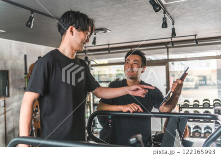 ランニングマシンで有酸素運動をする男性と指導するパーソナルトレーナーの男性 122165993