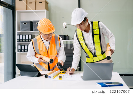 Contractor and architect looking at plan, tablet, laptop and talking about working on big project. Contractor and architect looking at plan, tablet, laptop and talking about working on big project. 122167007