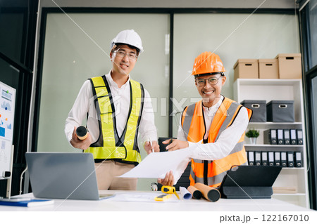 Contractor and architect looking at plan, tablet, laptop and talking about working on big project. 122167010