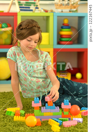 Portrait of cute girl playing with colorful plastic blocks in room 122167445