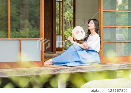 古民家の縁側に座って、団扇で扇いで涼む若い女性 古民家の縁側に座って、団扇で扇いで涼む若い女性 122167892