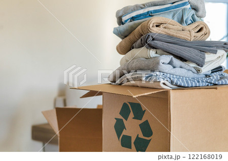 Pile of clothes in cardboard box donating for recycling reusing at living room with houseplant Pile of clothes in cardboard box donating for recycling reusing at living room with houseplant 122168019