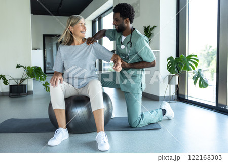 Male physiotherapist assisting female patient with therapy exercises for shoulder trauma recovery Male physiotherapist assisting female patient with therapy exercises for shoulder trauma recovery 122168303