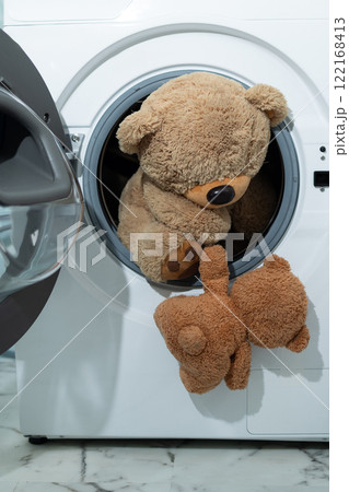 A cute teddy bear is peeking its head out of a washing machine 122168413