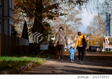 A loving couple strolls through a sunlit park with their young son, surrounded by the vibrant colors of autumn, enjoying a joyful and peaceful family moment together. 122172015