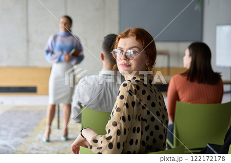 A diverse group of business professionals sits attentively in a modern office, actively participating in a training session led by an instructor, focusing on the latest technological advancements in 122172178