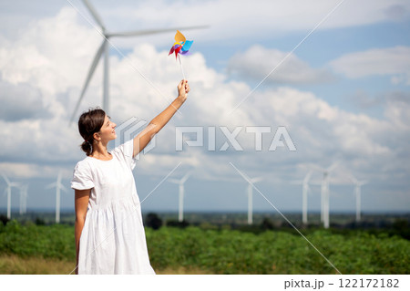 Young caucasian woman holding pinwheel in wind farm with turbines in blue sky nature. 122172182