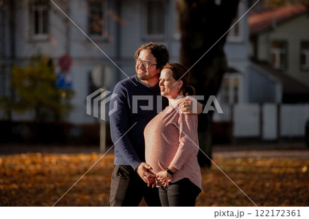 A man lovingly embraces his pregnant wife in the park, sharing a peaceful moment of warmth and affection  122172361