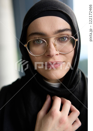 A stunning Muslim businesswoman is captured in a close-up portrait, showcasing her captivating green eyes behind stylish prescription glasses, radiating elegance and confidence 122172466