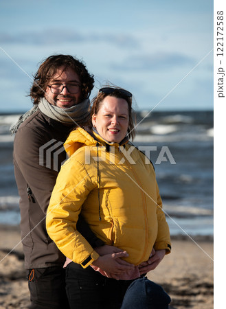 A couple stands embraced on a sandy beach on a chilly autumn day, the serene ocean stretching behind them as they share a quiet moment of love and warmth amidst the cool breeze and peaceful A couple stands embraced on a sandy beach on a chilly autumn day, the serene ocean stretching behind them as they share a quiet moment of love and warmth amidst the cool breeze and peaceful 122172588