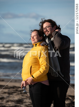 A couple stands embraced on a sandy beach on a chilly autumn day, the serene ocean stretching behind them as they share a quiet moment of love and warmth amidst the cool breeze and peaceful A couple stands embraced on a sandy beach on a chilly autumn day, the serene ocean stretching behind them as they share a quiet moment of love and warmth amidst the cool breeze and peaceful 122172668